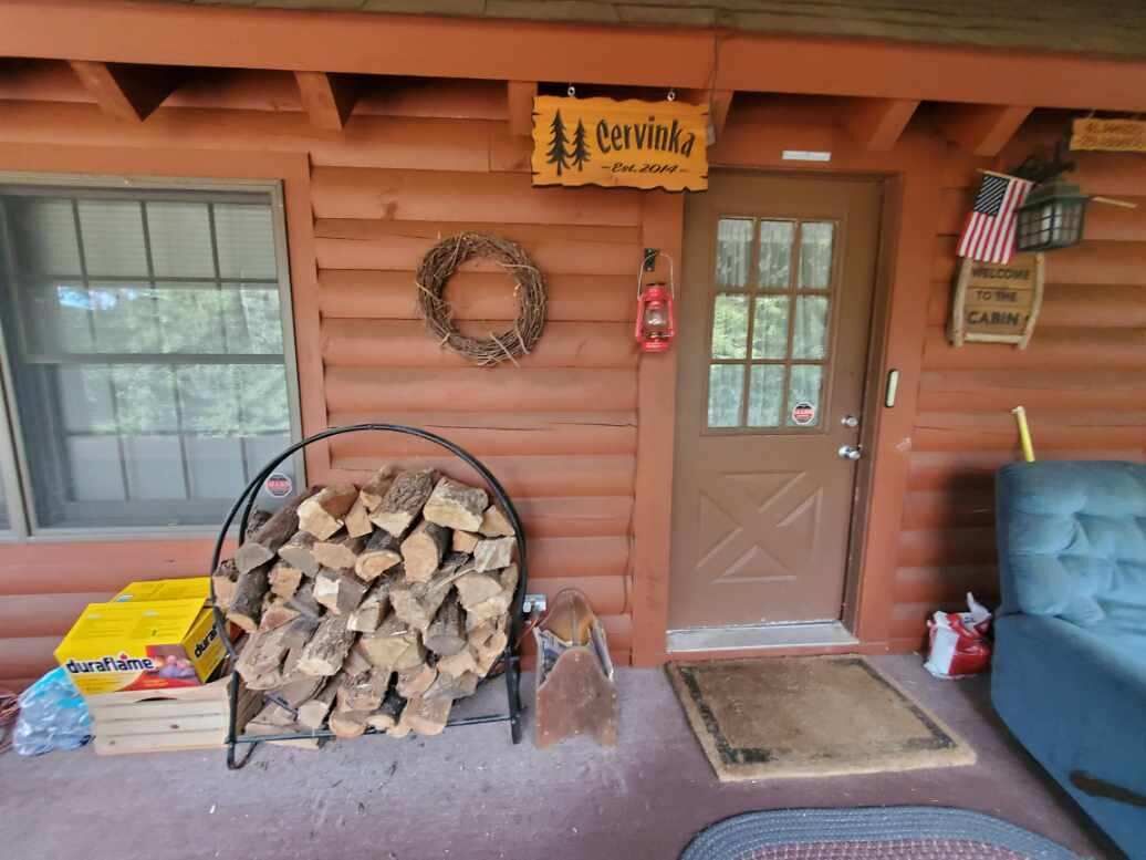 L’entrée d’un chalet, avec une porte, une guirlande, une pile de bois de chauffage, une pancarte de bienvenue et un canapé bleu.