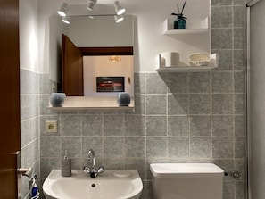 Une salle de bain équipée d’un lavabo, de toilettes, d’un miroir et d’étagères où sont rangés les articles de toilette.