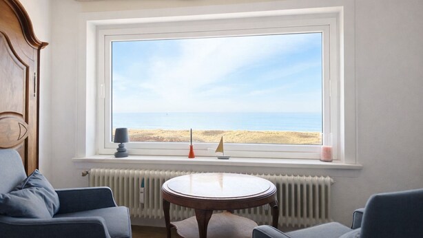 A room with a large window overlooking a beach, a round table, and two chairs.