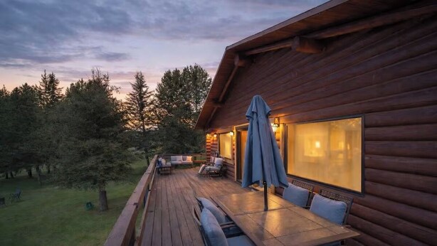 Una cabaña de madera con terraza, mobiliario exterior y ventanas amplias.