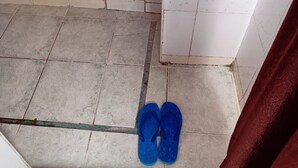 Un baño con lavamanos, paredes de azulejos y un par de pantuflas azules en el suelo.