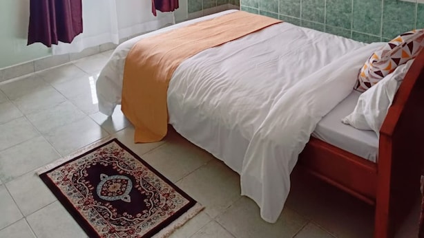 Un dormitorio con cama, mesita de noche, cortinas en la ventana y una lámpara de pared.