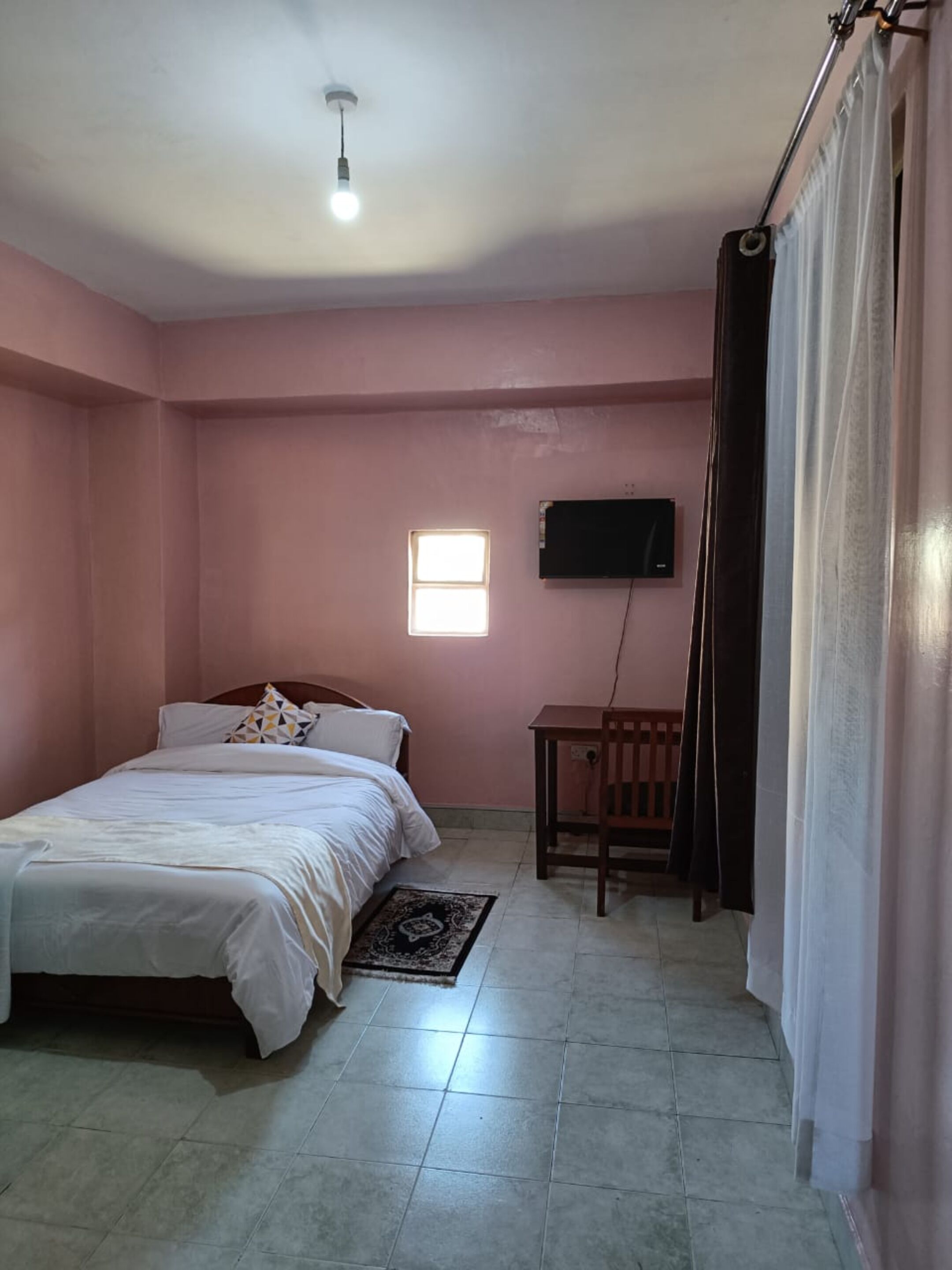 A bedroom with a bed, a small table, a TV, and a window.