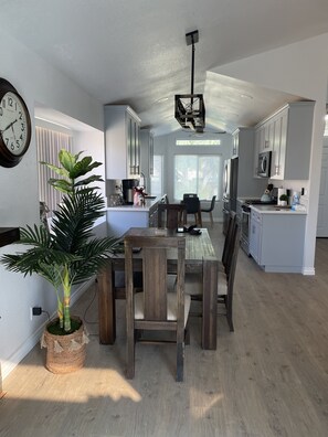 Une cuisine moderne avec des meubles blancs, un coin repas avec des meubles en bois et une grande plante en pot.