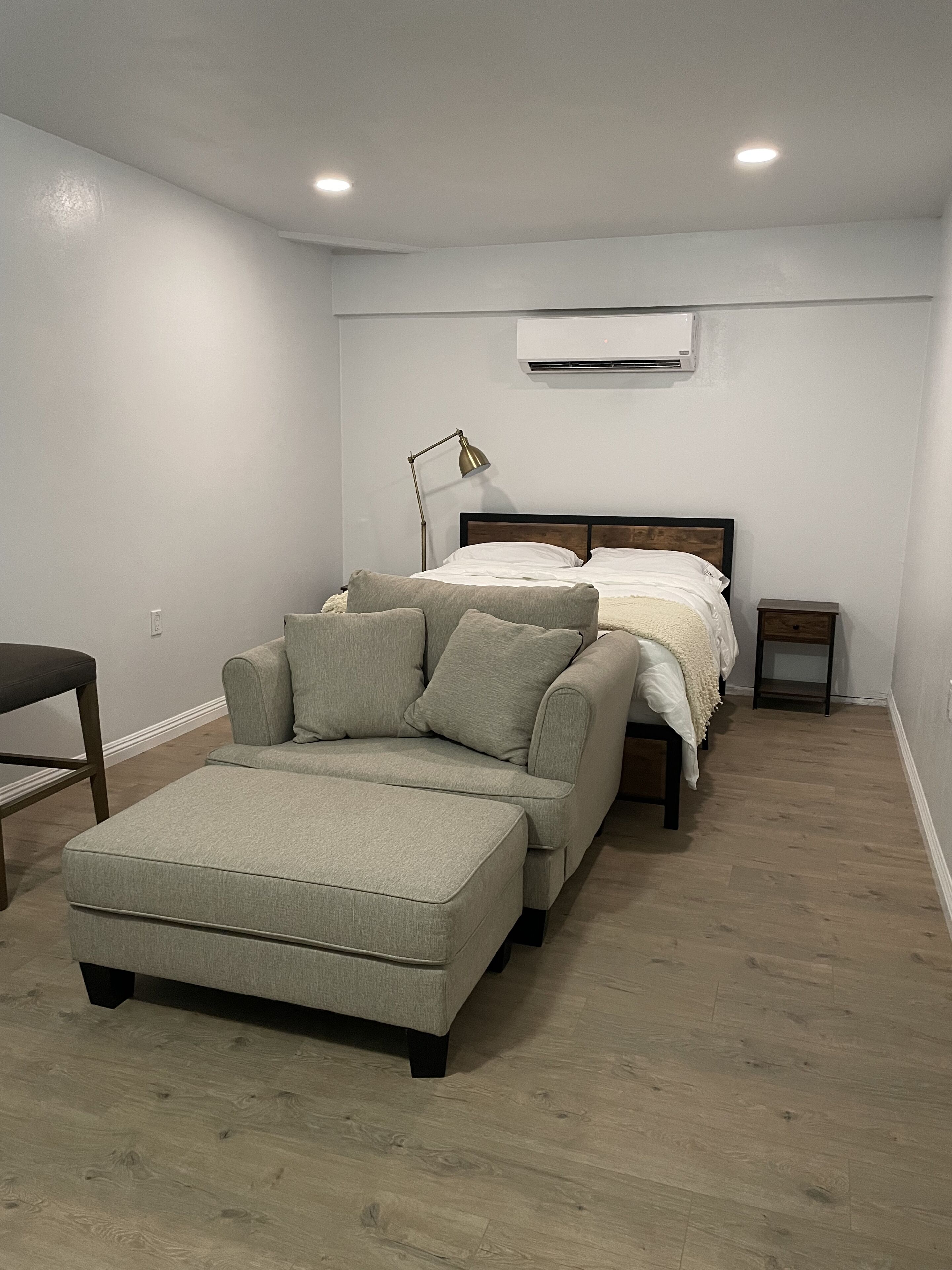 A bedroom with a bed, a nightstand, a lamp, and a sofa.