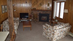 A cozy living room with wooden walls, a fireplace, a television, and floral-patterned sofas.