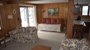 A cozy living room with a sofa, a wooden coffee table, and a bed with red pillows.