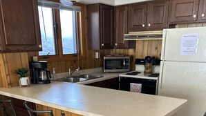A kitchen with a large island, wooden cabinets, a refrigerator, a microwave, and bar stools.
