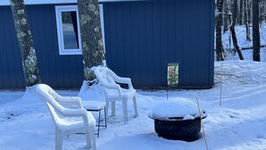 A snow-covered outdoor area with two white plastic chairs and a black trash bin.