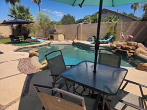 Un jardin avec une piscine, des meubles de patio et un espace barbecue.