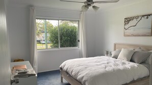 A bedroom with a bed, a desk with a laptop, and a window with curtains.