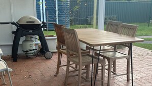 A patio with a wooden table and chairs, a grill, and a gas cylinder.