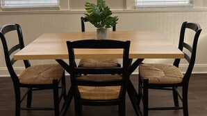 A dining area with a rectangular wooden table, four black chairs with woven seats, and a potted plant in the center.