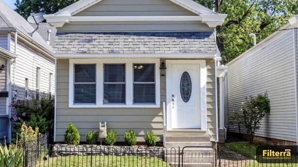 A single-story house with a front porch, a garage door, and a small garden with a fence.