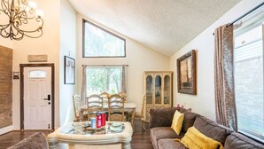 A cozy living room with a fireplace, a dining area with a wooden table and chairs, and a large window with curtains.