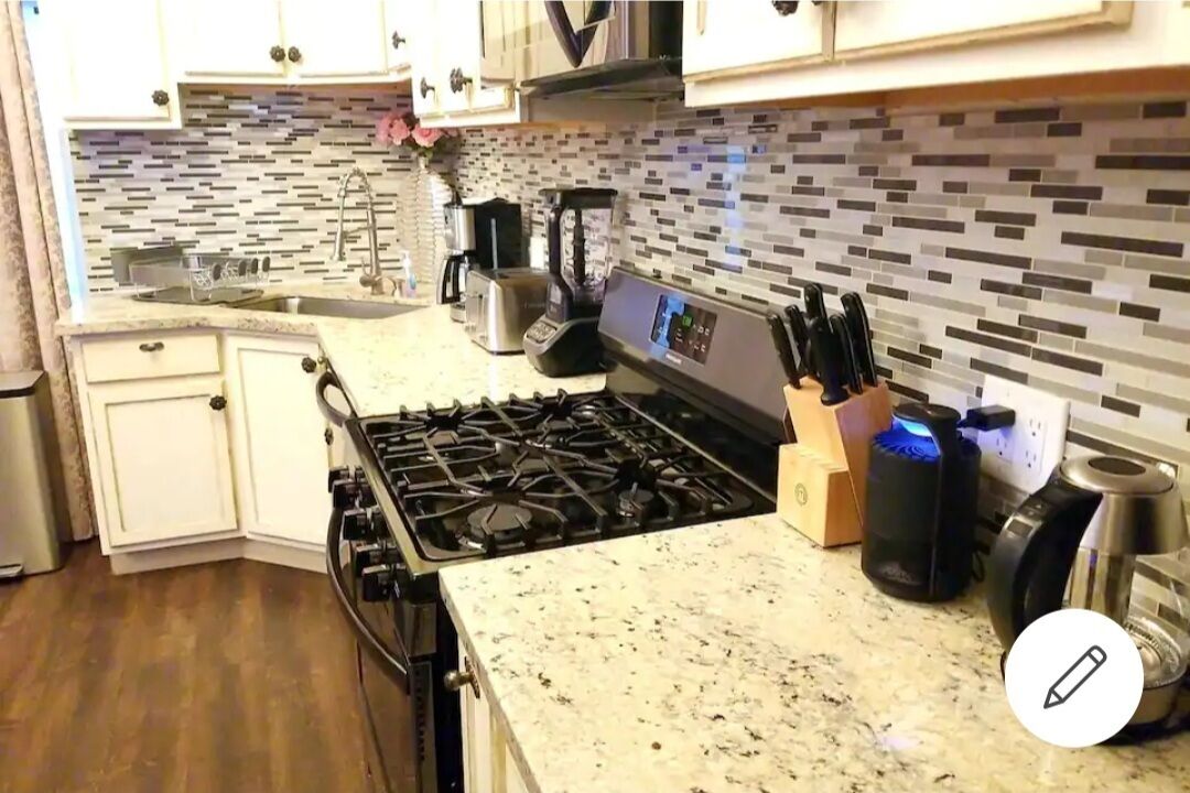 A kitchen with white cabinets, a gas stove, a coffee maker, and a blender.