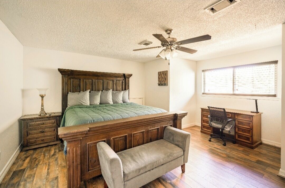 A bedroom with a wooden bed, a bench, a desk, and a ceiling fan.