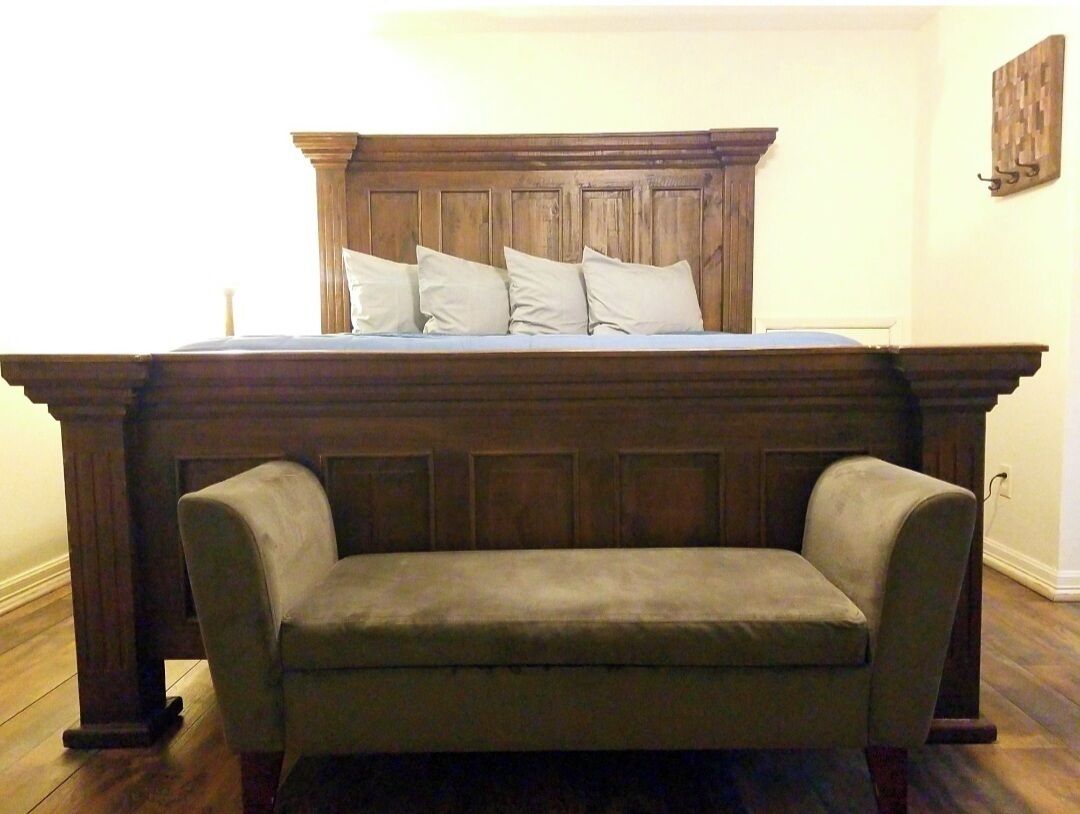 A bedroom with a large bed, a wooden headboard, and a bench at the foot of the bed.
