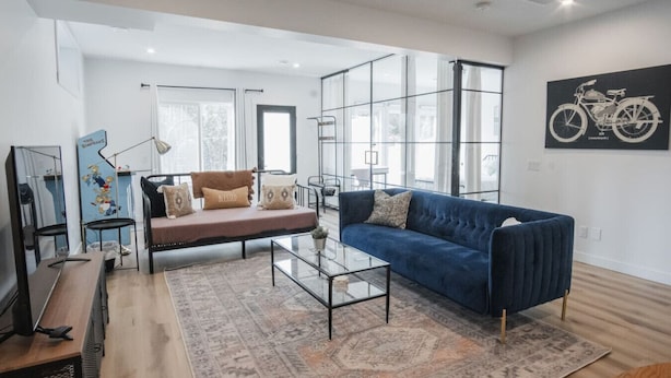 Een moderne woonkamer met een blauwe bank, een glazen salontafel en een kamerkleed met patroon.