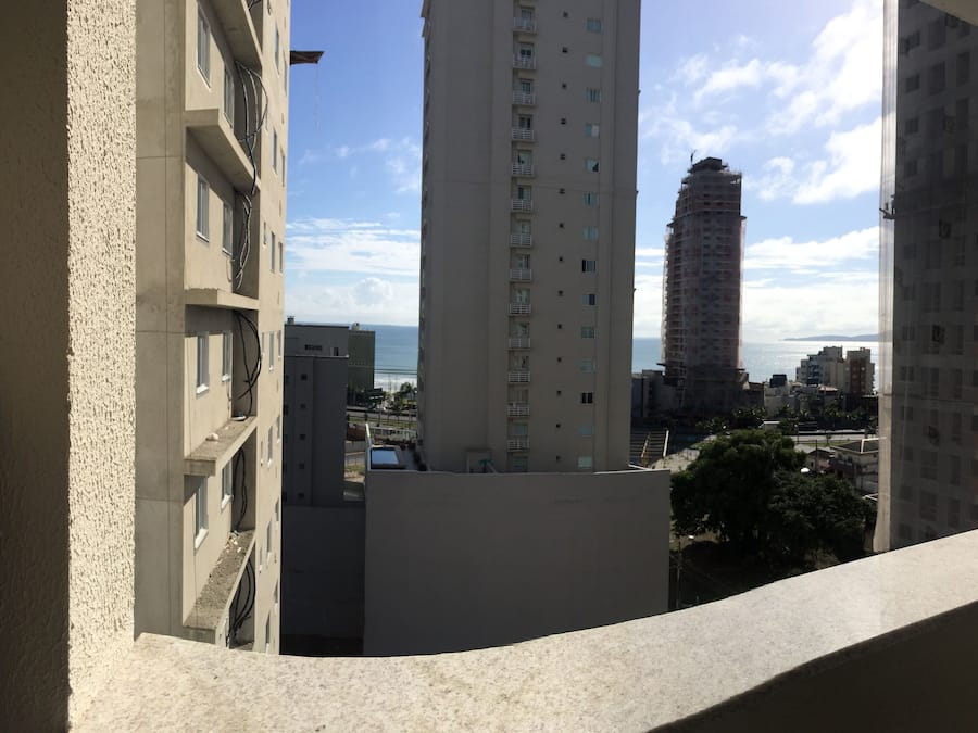 Vista de un edificio alto con balcón, otros edificios y una lejana vista al océano.