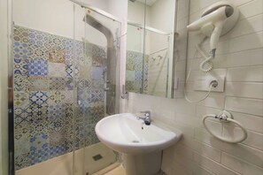 Un baño con pared de azulejos estampados, un lavabo blanco, un secador de pelo de mano y una mampara de cristal para la ducha.