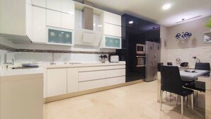 A modern kitchen with white cabinets, a built-in oven, and a dining area with a black chair and table.