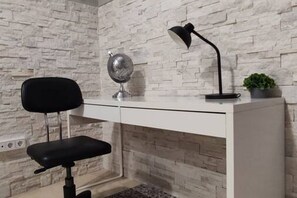 Un escritorio con una silla negra, un globo terráqueo, una lámpara y una pequeña planta.