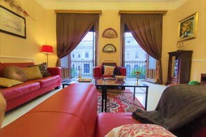 Una sala de estar con un sofá rojo, un sillón negro, una mesa de centro de vidrio y vistas a un edificio a través de amplias ventanas.