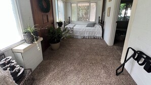 A bedroom with a bed, two potted plants, a window with blinds, a door with a wreath, and a carpeted floor. - Charming 3-bedroom house in Decatur City, Minutes from Little River Lake. (Decatur City)
