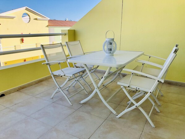 Ein Balkon mit einem weißen Tisch und Stühlen, einem weißen Laternen und einer gelben Wand.