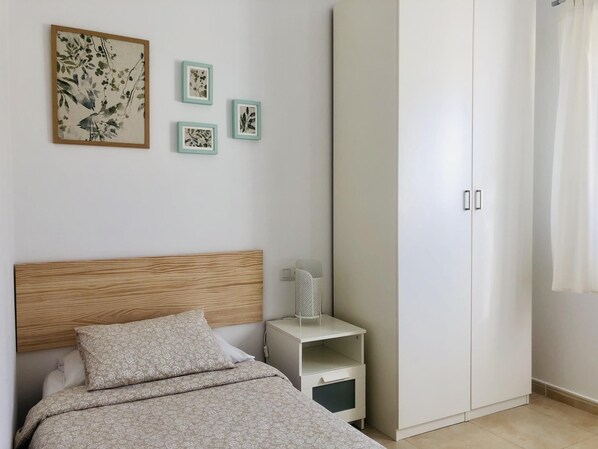 A bedroom with a bed, a nightstand, a wardrobe, and three framed pictures on the wall.
