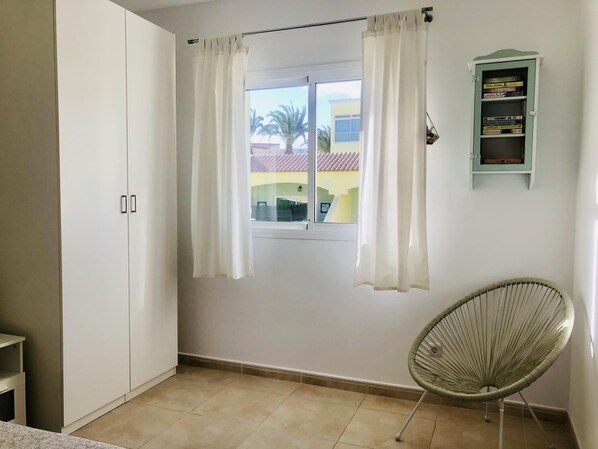 A room with a window, white curtains, a wicker chair, a cabinet with books, and a tiled floor. - COCO - Oasis of calm (Costa Calma (incl. Urbanización Cañada d)