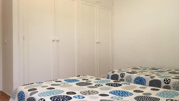 Une chambre avec deux lits, chacun recouvert d’une couvre-lit à motifs. On y trouve une armoire blanche à trois portes.