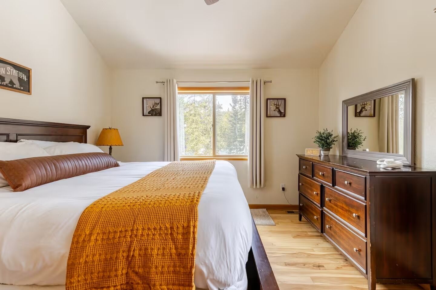 Een slaapkamer met een groot bed, een dressoir, een spiegel en een raam met gordijnen.