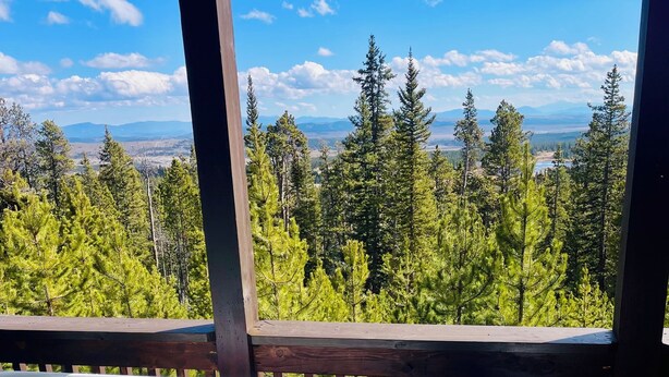 Un bain à remous avec une terrasse en bois et une vue sur une forêt et des montagnes.