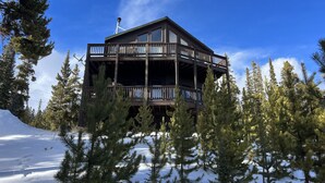 Un chalet à plusieurs étages doté d’un balcon, entouré de neige et de pins.