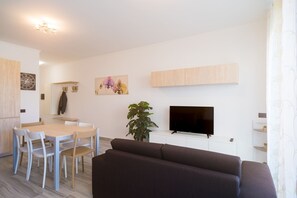 Una sala de estar moderna con un televisor de pantalla plana, un sofá marrón oscuro, una mesa de comedor con sillas y una planta en maceta.