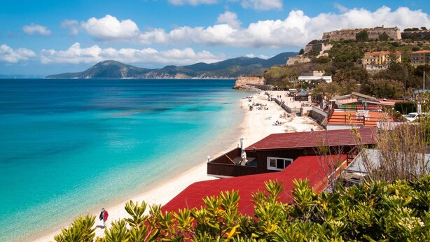 Un pueblo costero con una playa, edificios y una colina con ruinas.