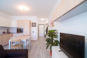 Una cocina moderna con armarios de madera, un comedor con mesa y sillas, un televisor de pantalla plana grande y una planta en maceta.