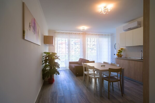 Un espace de vie compact comprenant un coin repas, une kitchenette et une grande fenêtre avec des rideaux.