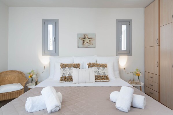 A bedroom with a bed, two bedside tables, a wicker chair, a wardrobe, and a starfish decoration on the wall.
