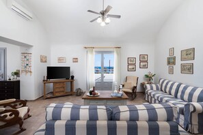 A living room with a large TV, striped sofa, and a view of the sea through a balcony door.