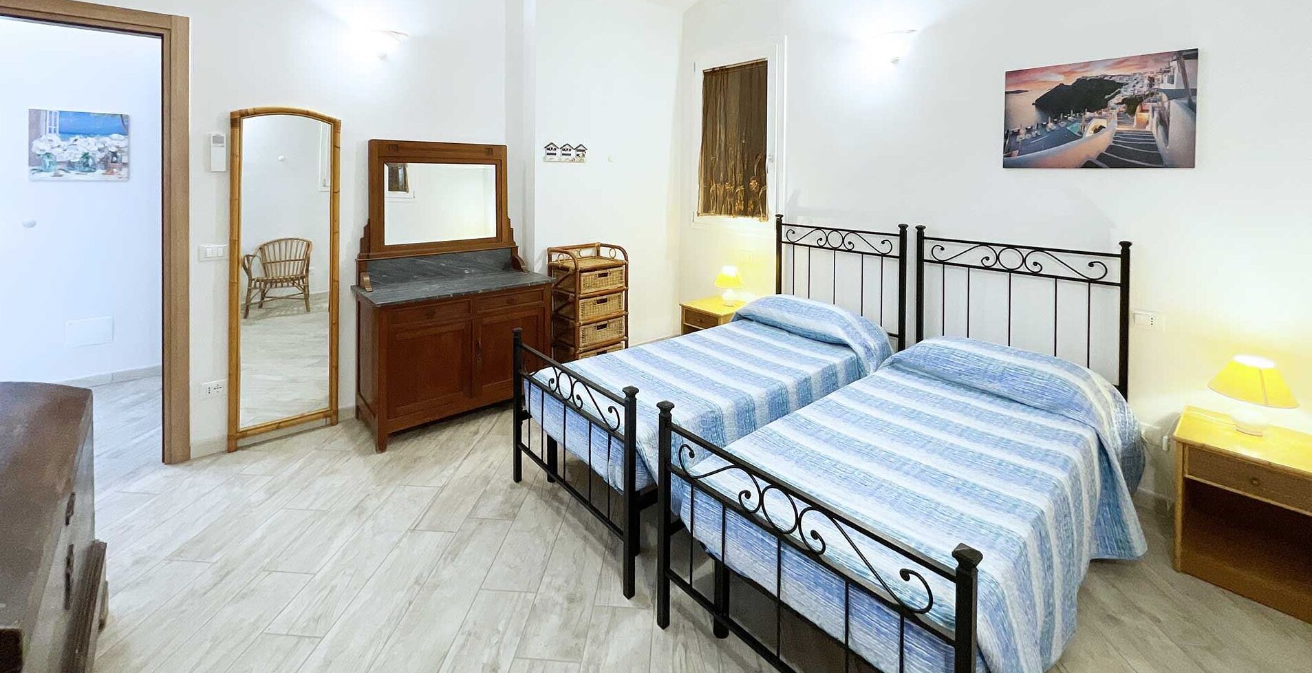 A bedroom with two beds, a wooden dresser, a mirror, and a painting on the wall.