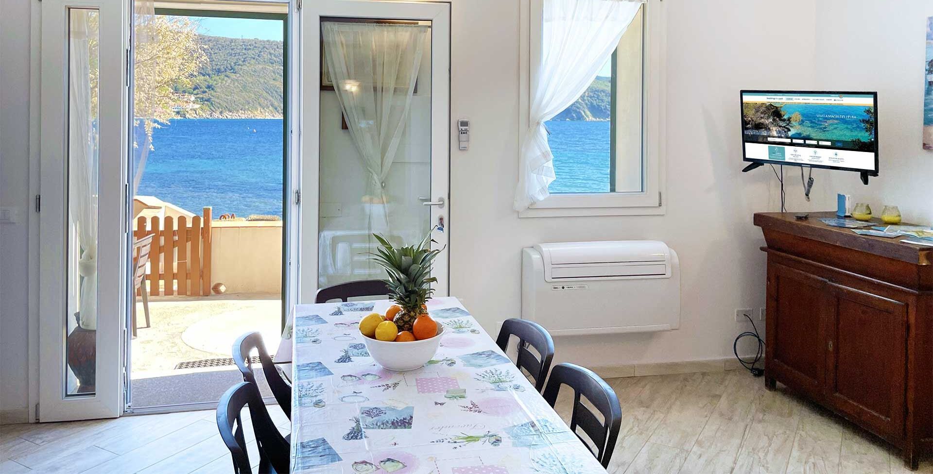 Ein Essbereich mit einem Tisch für zwei Personen, einer Obstschale und Blick auf das Meer durch eine Glastür.