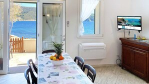 Un comedor con una mesa dispuesta para dos personas, un frutero y vista al mar a través de un ventanal.