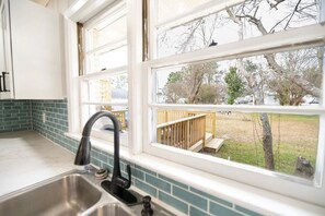 A kitchen with a stainless steel sink, a window with a view of a backyard with a wooden deck and trees. - 3 BR/ 2 Bath king, Fire Pit (Edenton)