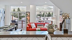 Una sala de estar moderna con un sofá rojo, ventanas grandes y vistas a montañas.
