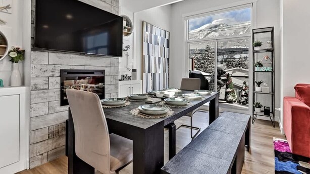 Un moderno comedor con chimenea, un televisor de pantalla plana grande y vistas a montañas nevadas a través de amplios ventanales.