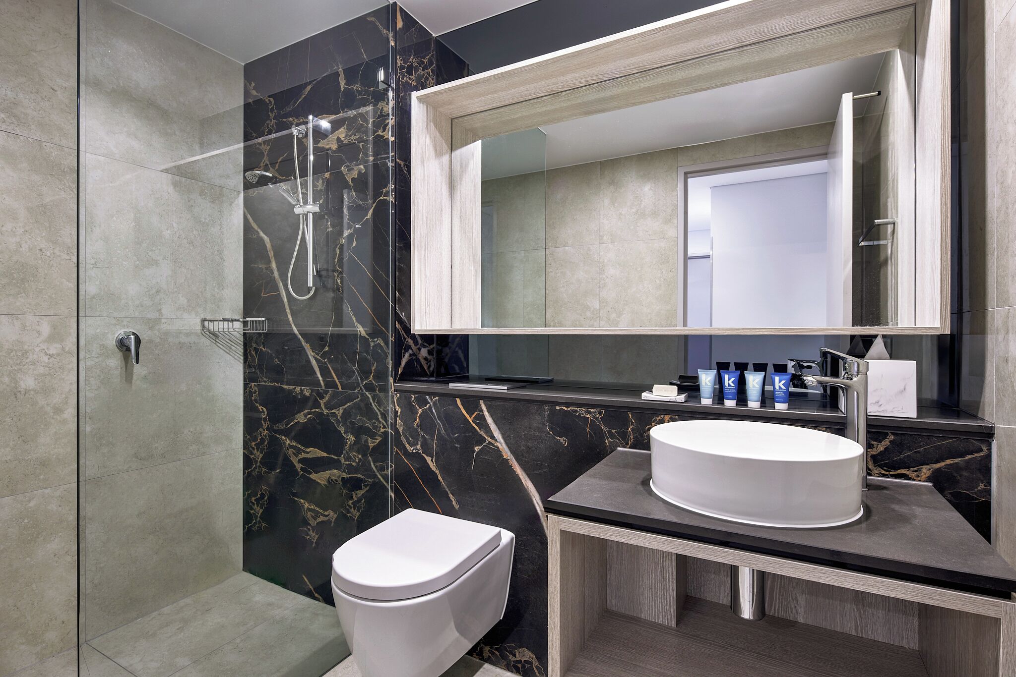 Une salle de bain moderne avec une douche à parois de verre, des toilettes blanches et un meuble-lavabo doté d’un grand miroir et d’un évier.