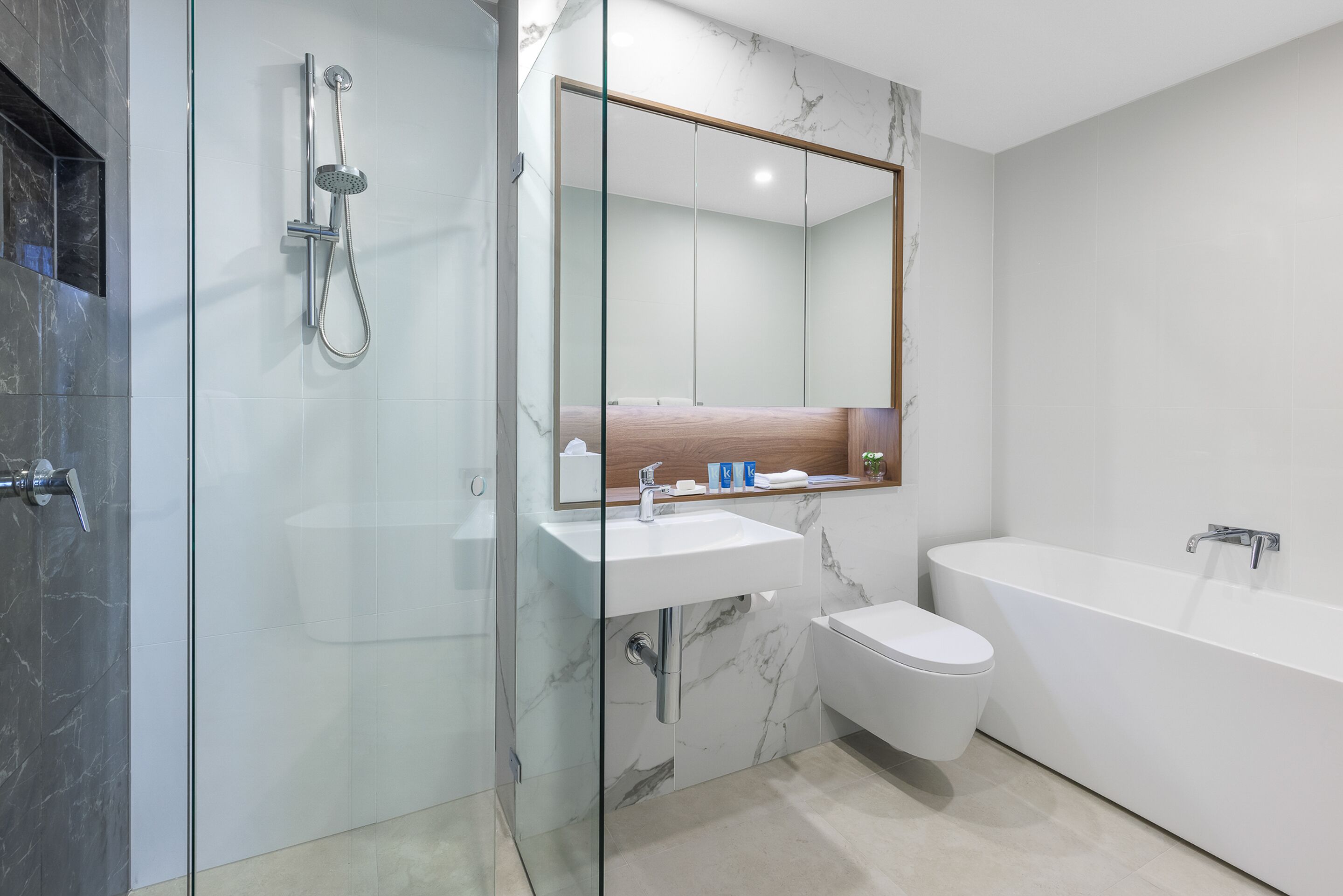 A modern bathroom with a glass-enclosed shower, a marble sink, a toilet, and a freestanding bathtub.